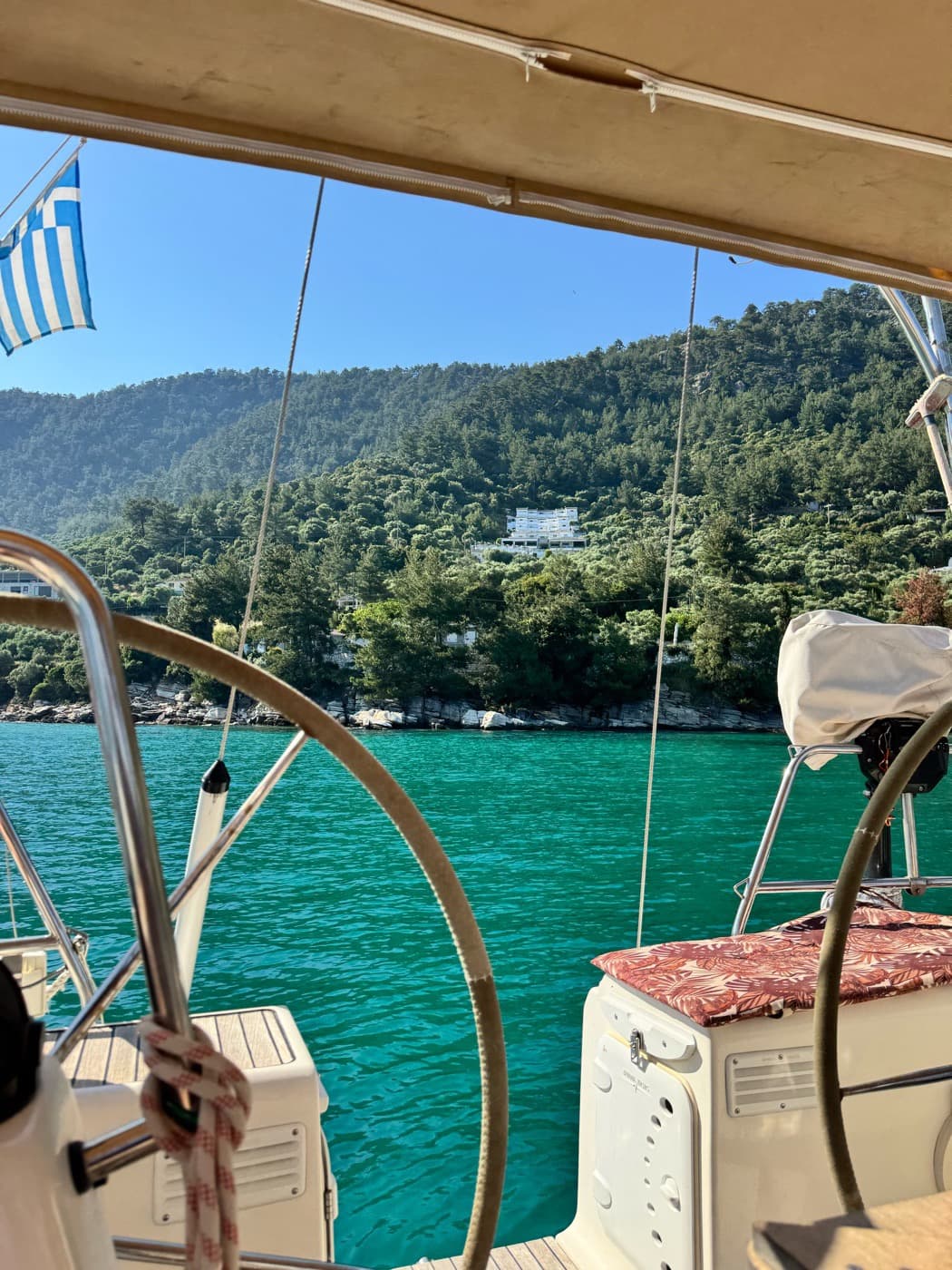 The helm and the Greek flag above a green bay