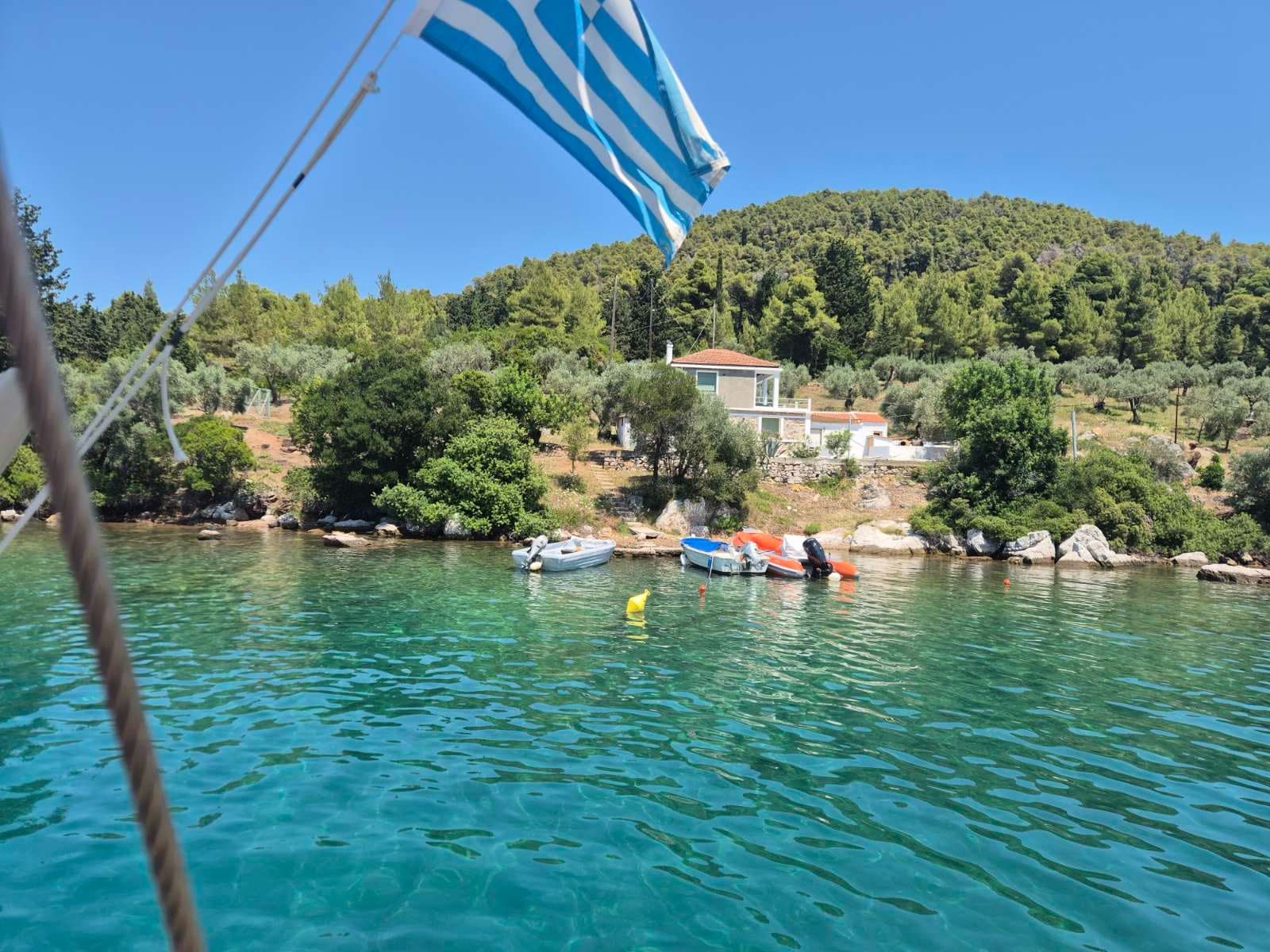 The Greek flag at the stern above a calm bay with small boats