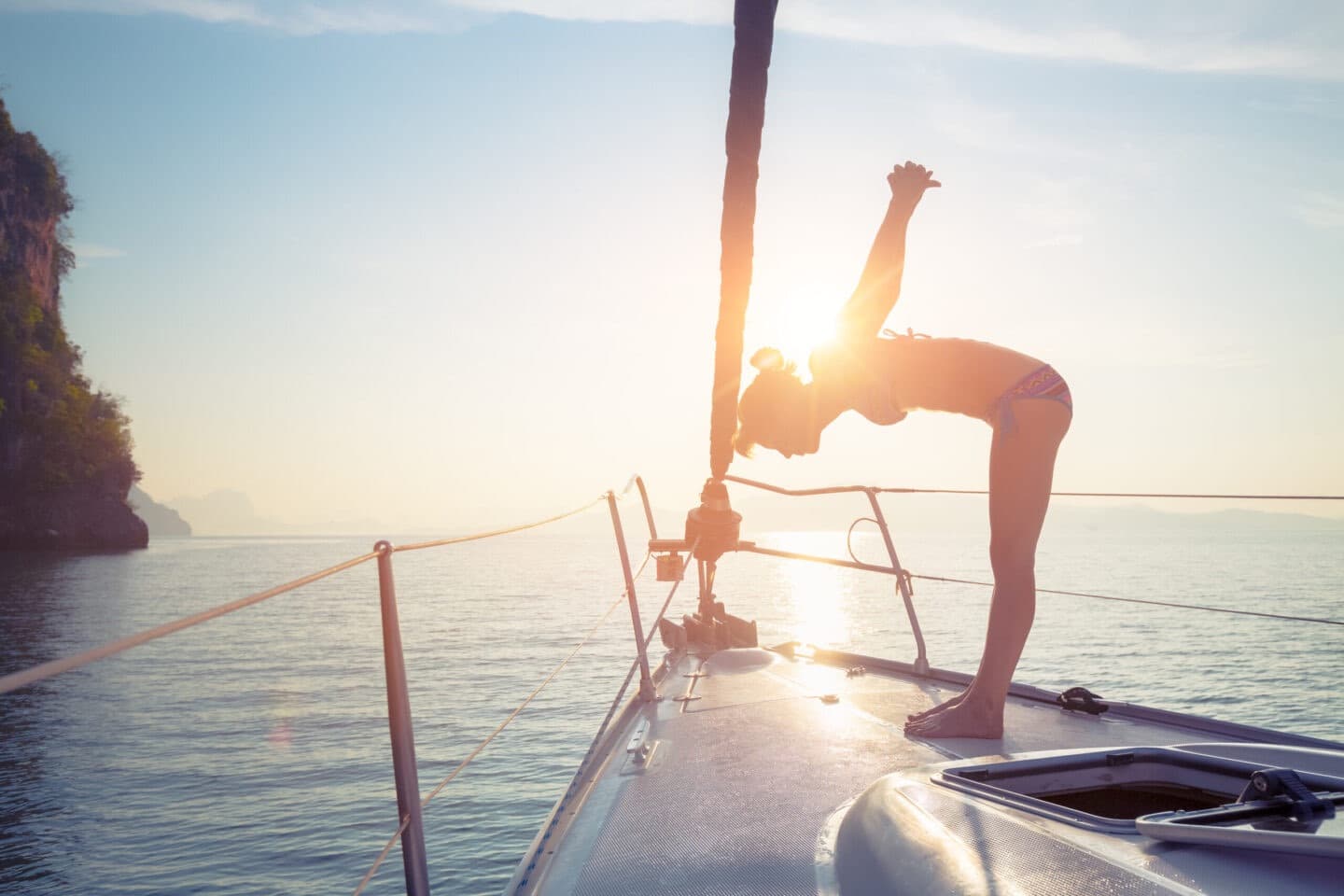 A woman stretching in a pilates pose on the bow of a yacht at sunset