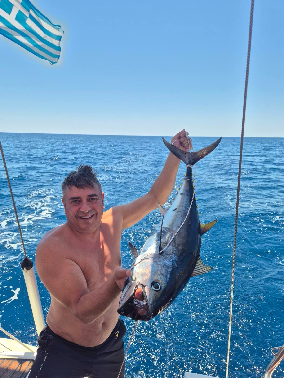 A fisherman on deck holding up a tuna caught on the trip