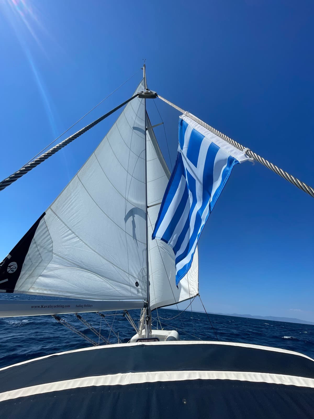 The Greek flag flying beside the full sails under a blue sky